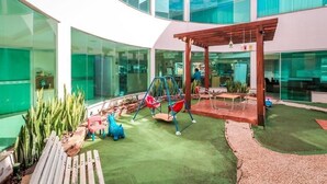 Un espace de jeux intérieur moderne, doté d’une balançoire en bois, d’un petit toboggan et d’un banc.