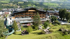 Een meerhoog hotel met een skilift op de voorgrond, omgeven door weelderige groene heuvels en een heldere lucht.