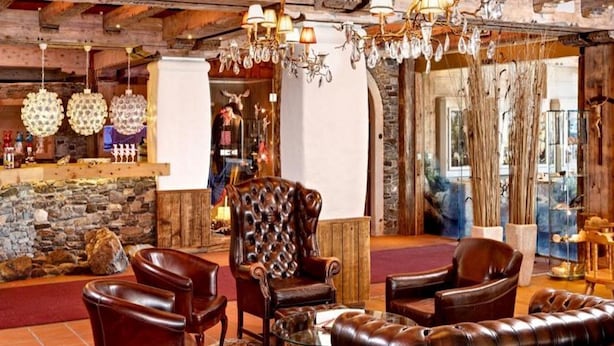 Een landelijk interieur met lederen meubels, stenen muren en kroonluchters.