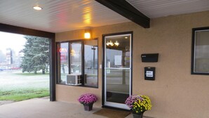 A building entrance with a glass door, a mail drop, and two flower pots. - Siesta Motel (Olds)