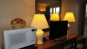 A microwave, a basket of fruit, and two lamps on a wooden desk in a hotel room. - Siesta Motel (Olds)