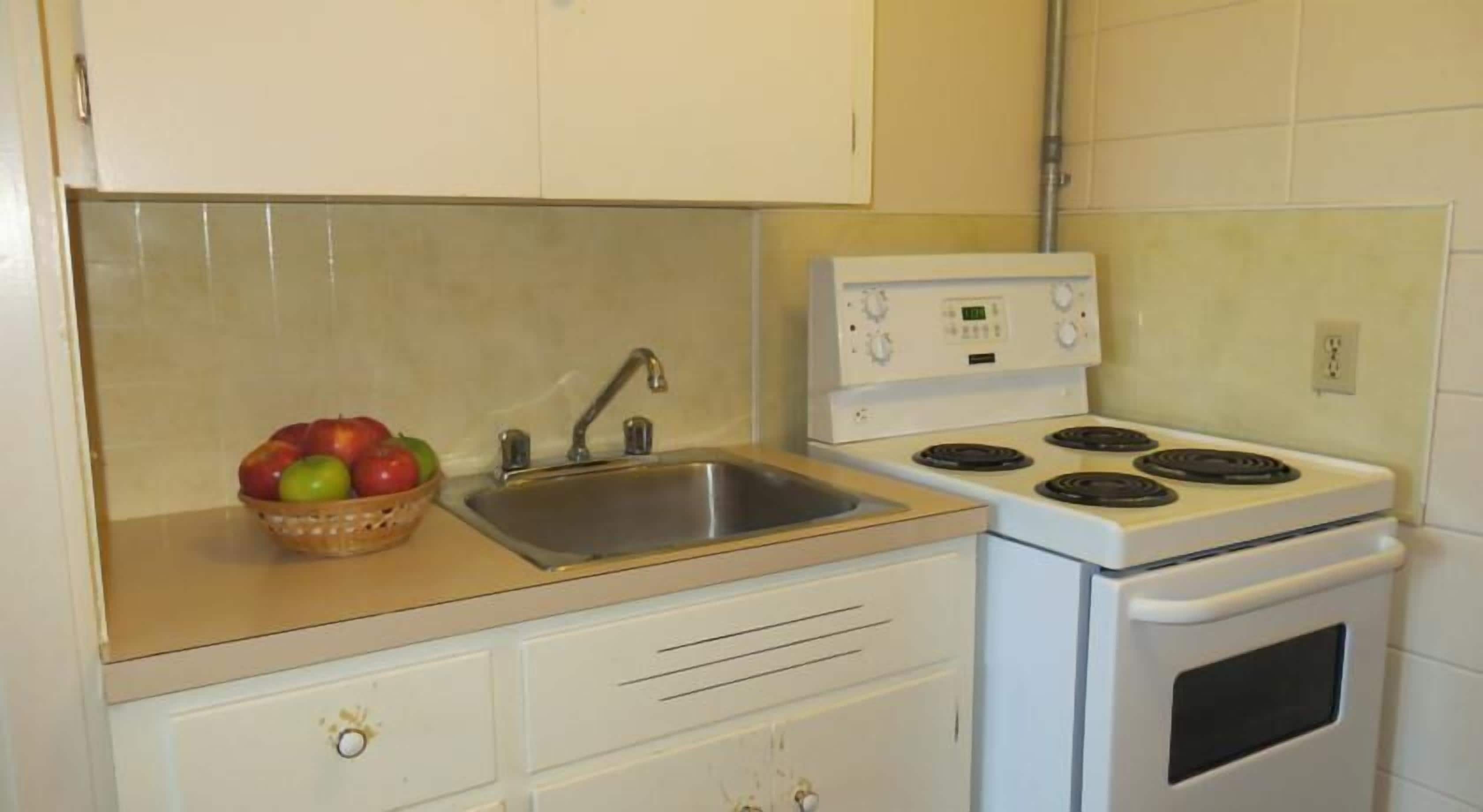 Una cocina con un lavamanos, estufa y una cesta de manzanas.
