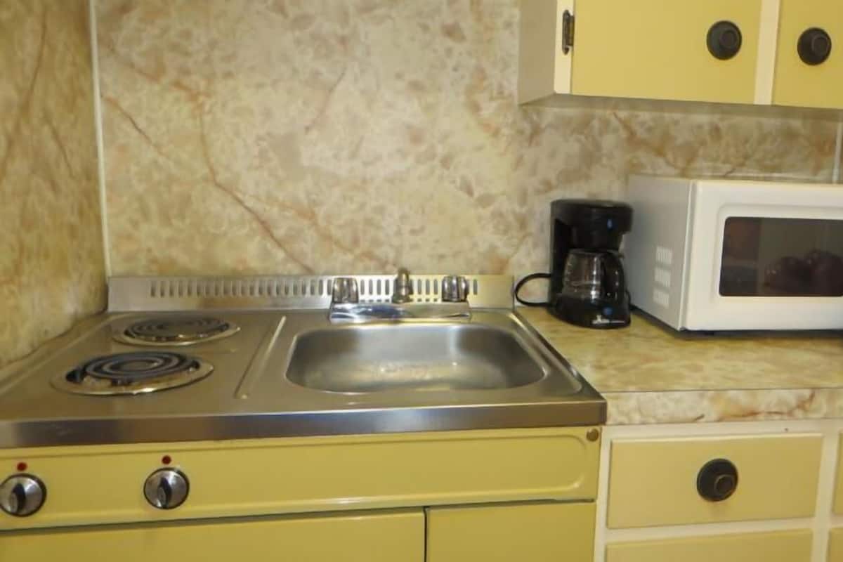 A kitchen with a stove, sink, microwave, and a basket of apples on the counter.