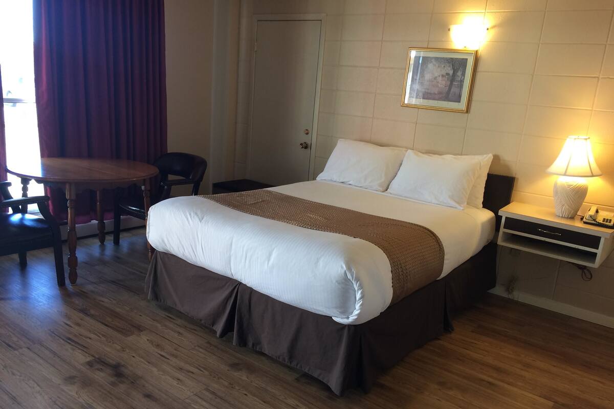 A neatly arranged hotel room with a large bed, a bedside table with a lamp, a chair, and a door.