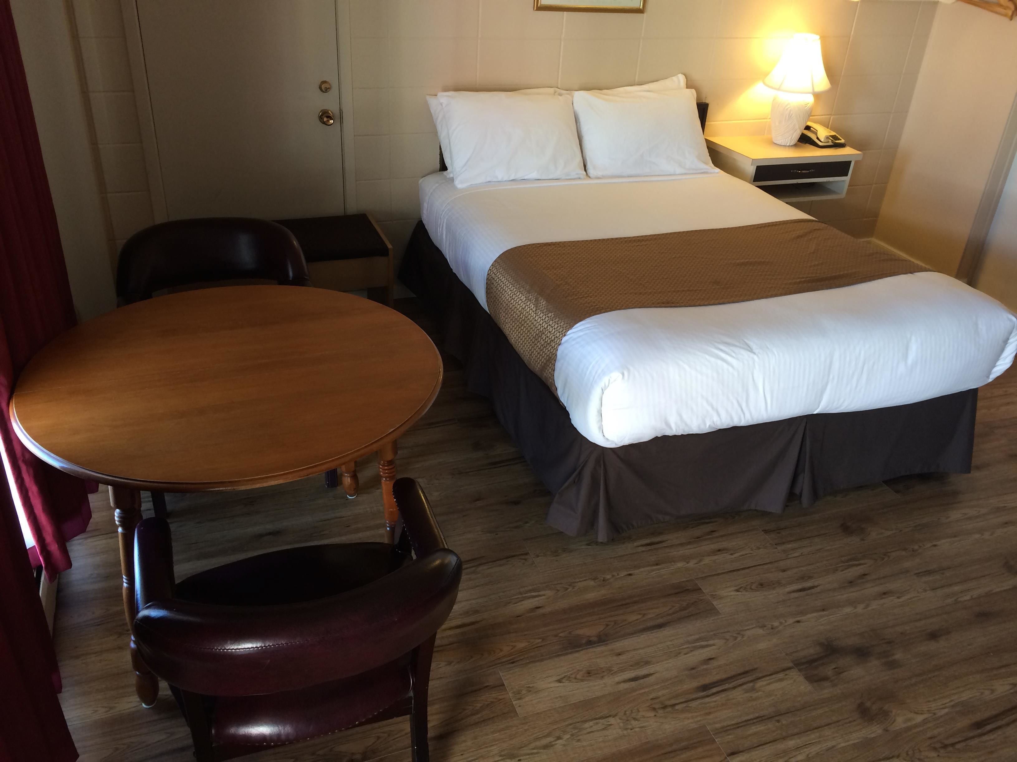 Een hotelkamer met een bed, nachtkastje, lamp en een houten stoel.
