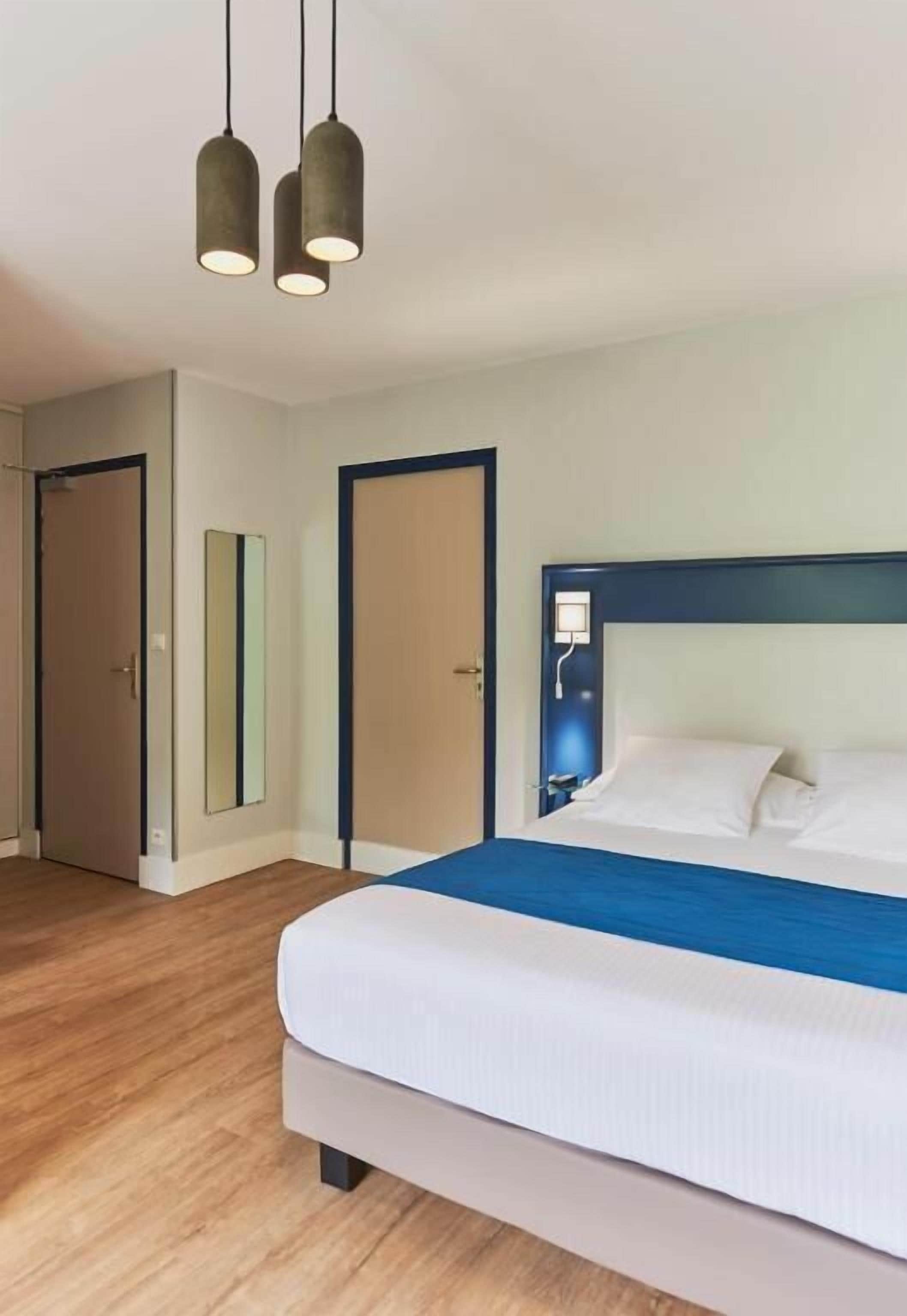 Une chambre d’hôtel avec un lit, deux lampes suspendues, une porte et un miroir.