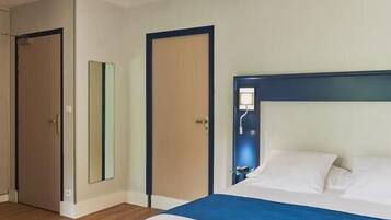 Une chambre d’hôtel avec un lit, deux lampes suspendues, une porte et un miroir.