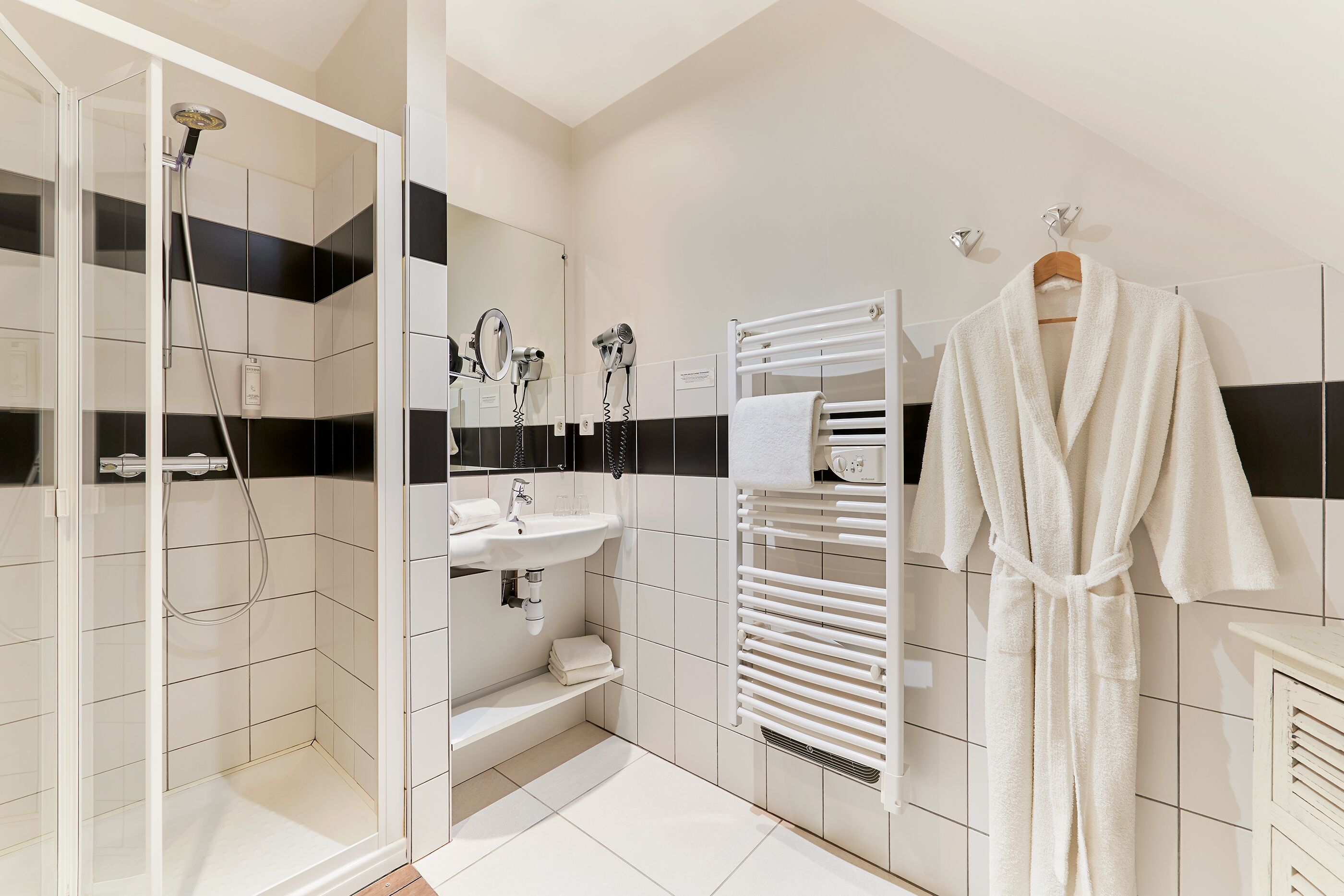 A modern bathroom with a glass-enclosed shower, a sink, a towel rack, and a robe hanging on a rack.