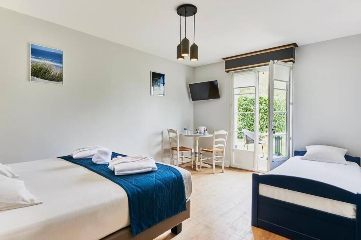 Une chambre d’hôtel avec deux lits, un bureau, une chaise, une télévision et une porte-fenêtre coulissante donnant sur un balcon.