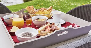 A breakfast tray with various food items and drinks, including bread, cheese, and a cup of coffee, set on a red tablecloth outdoors. - Hôtel Spa & Restaurant Les Saules (Favieres)