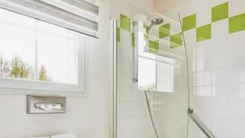 A modern bathroom with a glass-enclosed shower, a white sink, and a window with blinds.