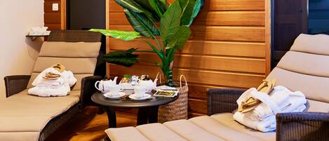 A cozy lounge area with wicker furniture, a large plant, and a table set with tea and towels.