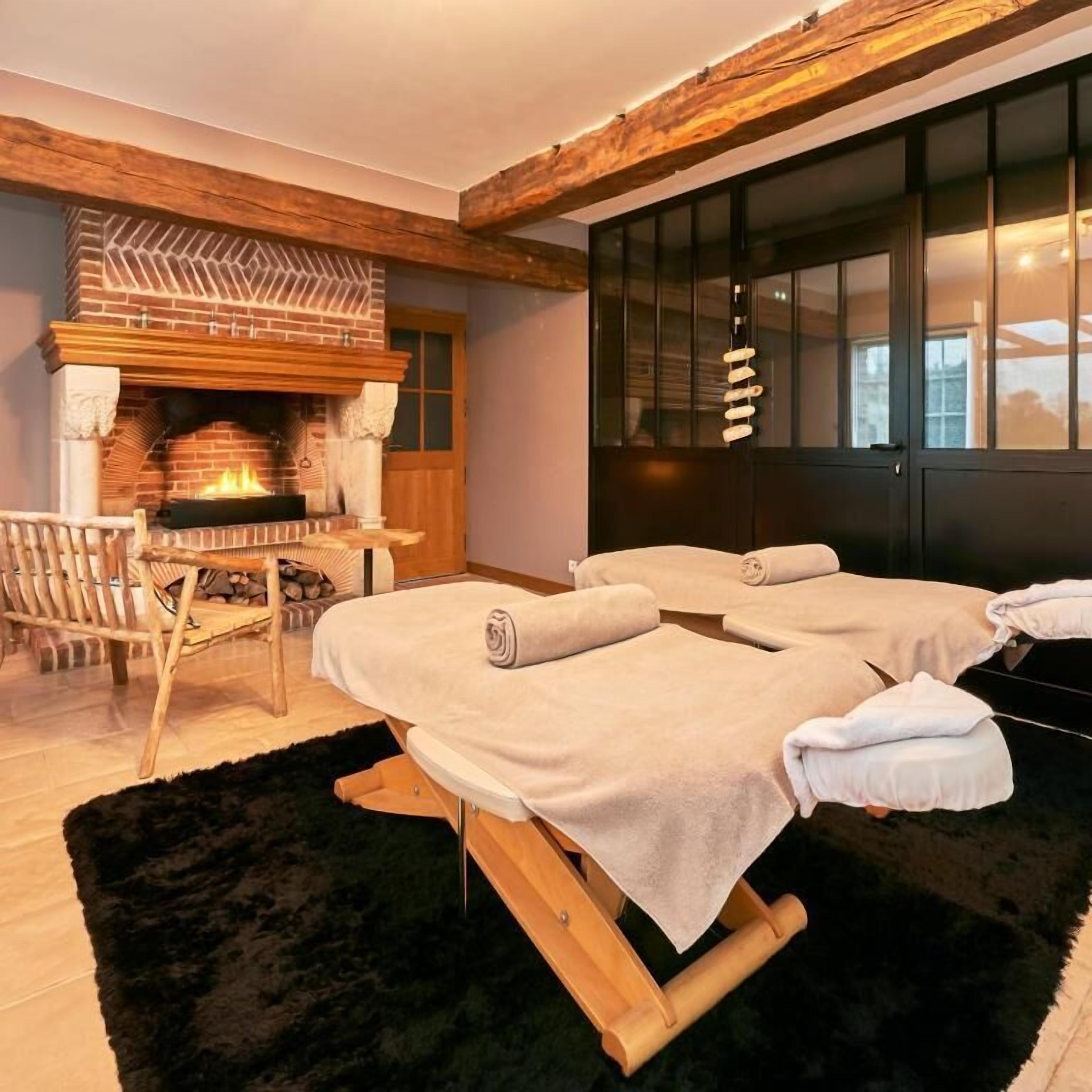 A spa room with a fireplace, wooden beams, and two massage tables.