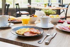 A breakfast table with plates of scrambled eggs, bacon, toast, and fruit. There are cups of coffee and a glass of orange juice. - Hôtel Spa & Restaurant Les Saules (Favieres)