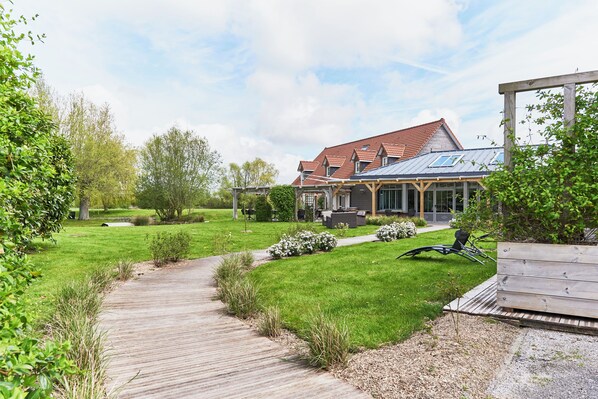 A house with a wooden deck, a lawn, and a covered outdoor area. - Hôtel Spa & Restaurant Les Saules (Favieres)