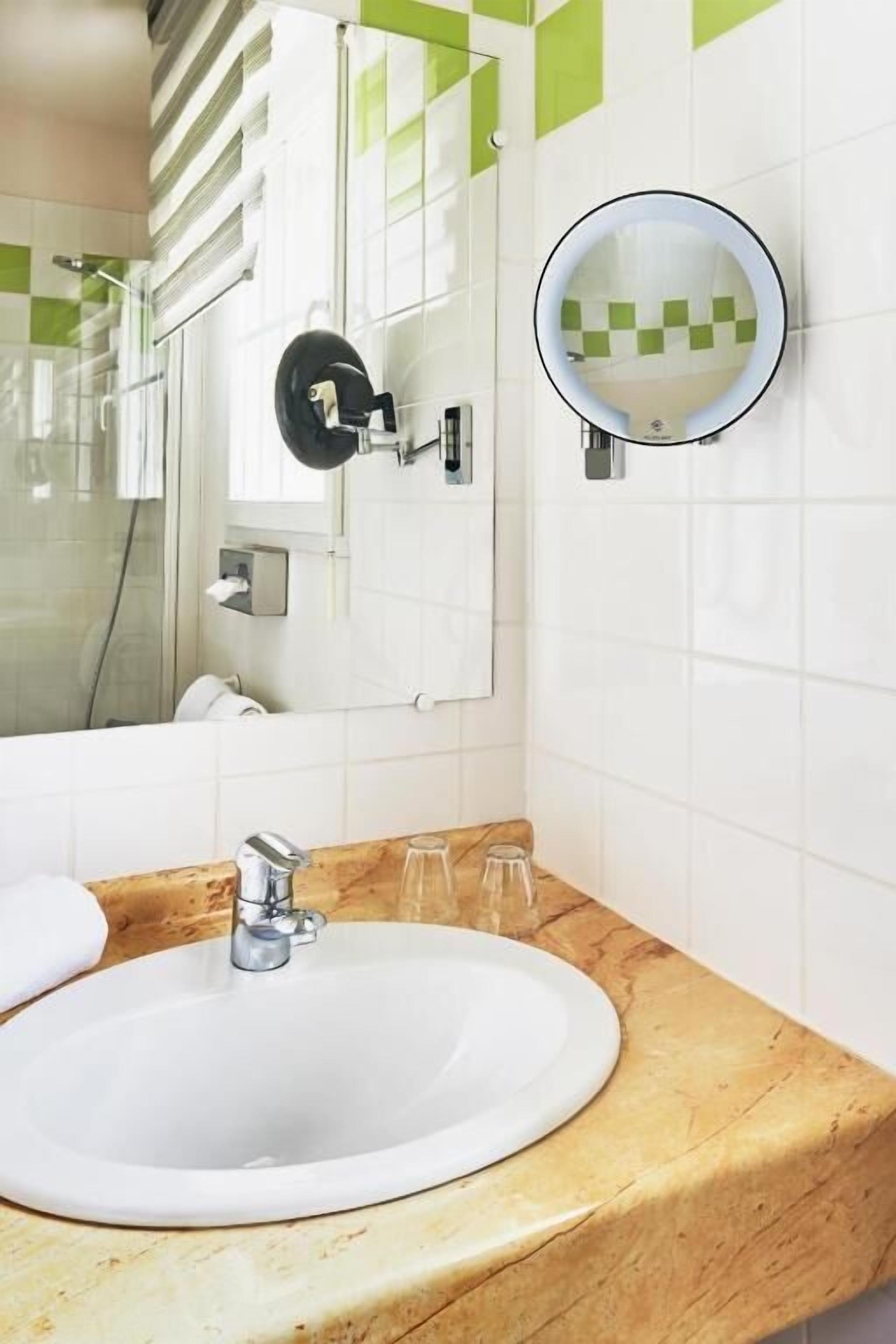 Un baño con un lavamanos blanco, un espejo redondo y una cabina de ducha de vidrio.