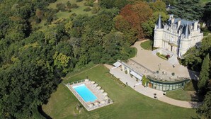 Vista aérea de una extensa propiedad con piscina, césped cuidado y un edificio imponente con múltiples torres.