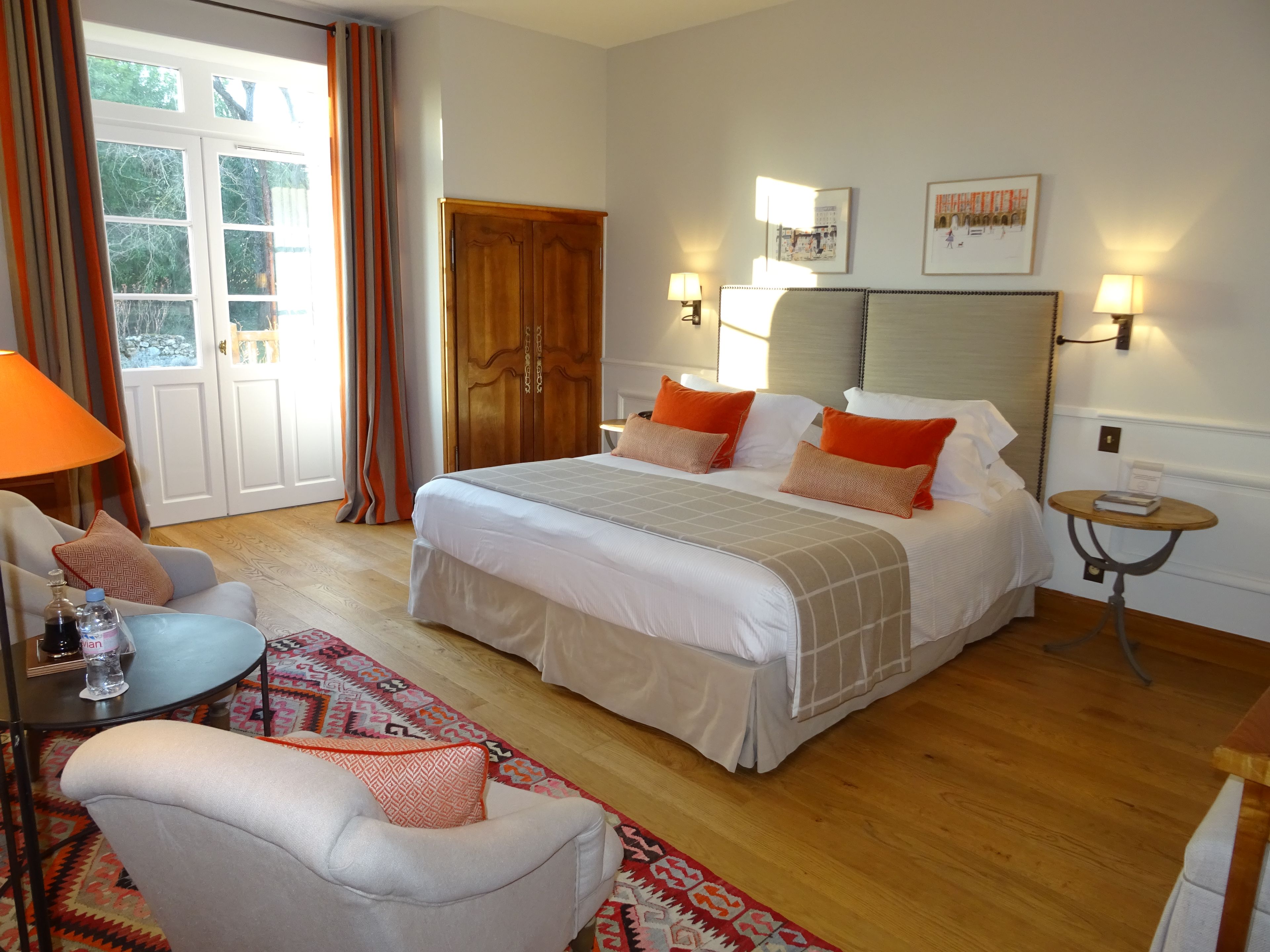 A hotel room with a bed, a chair, a small table, a lamp, and a door leading to a balcony.