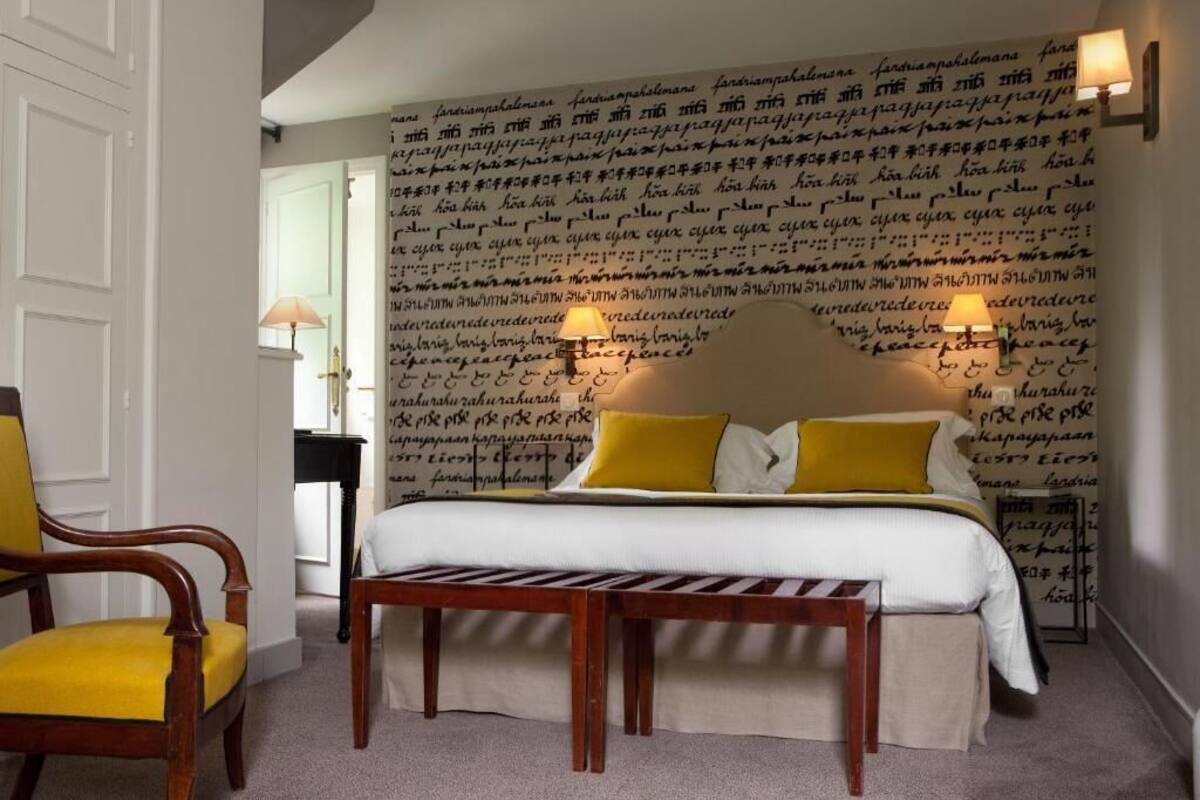 A bedroom with a bed, a wooden bench, a chair, and a lamp.