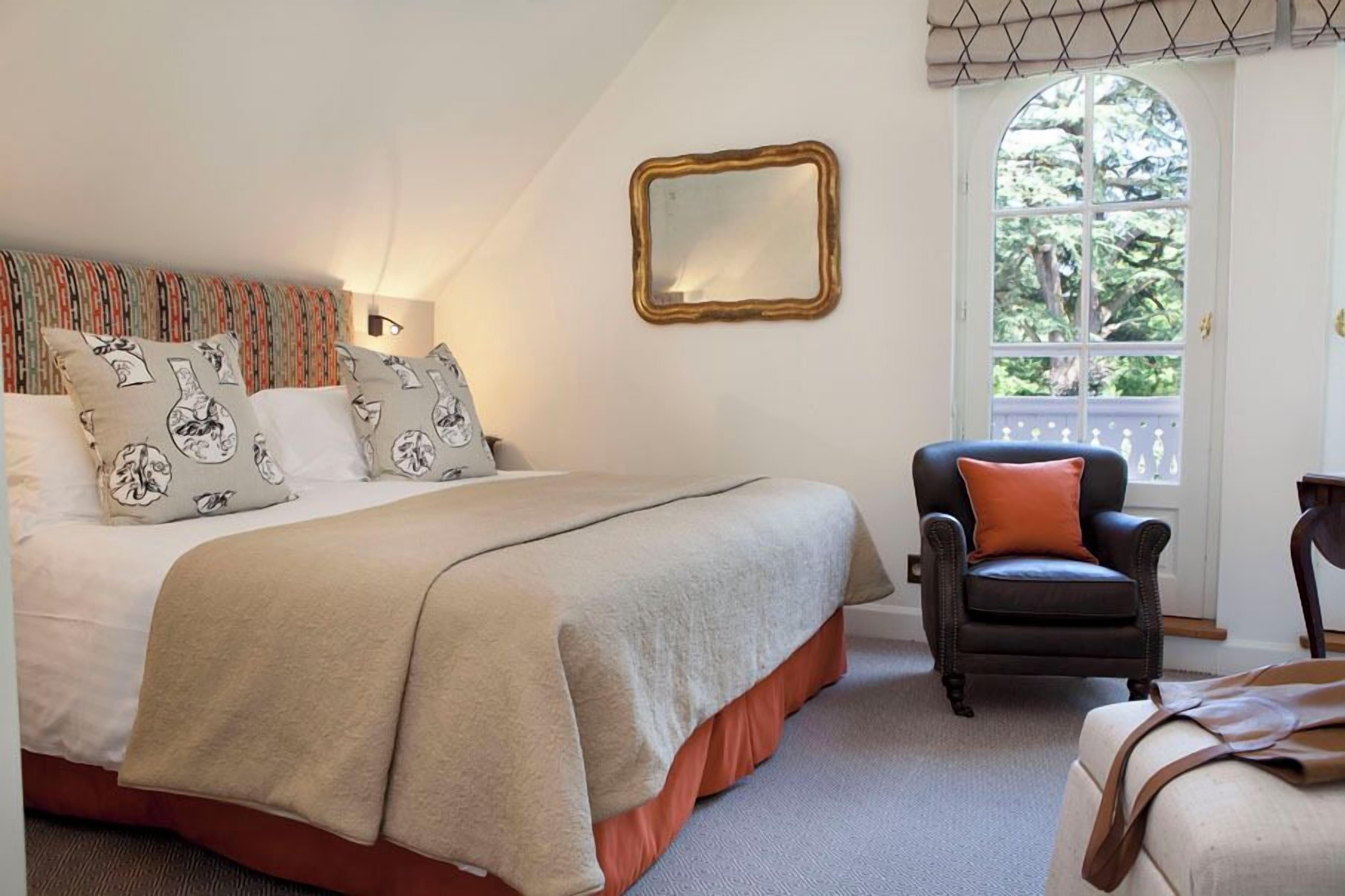 Ein Schlafzimmer mit Bett, Stuhl, Spiegel und Fenster.