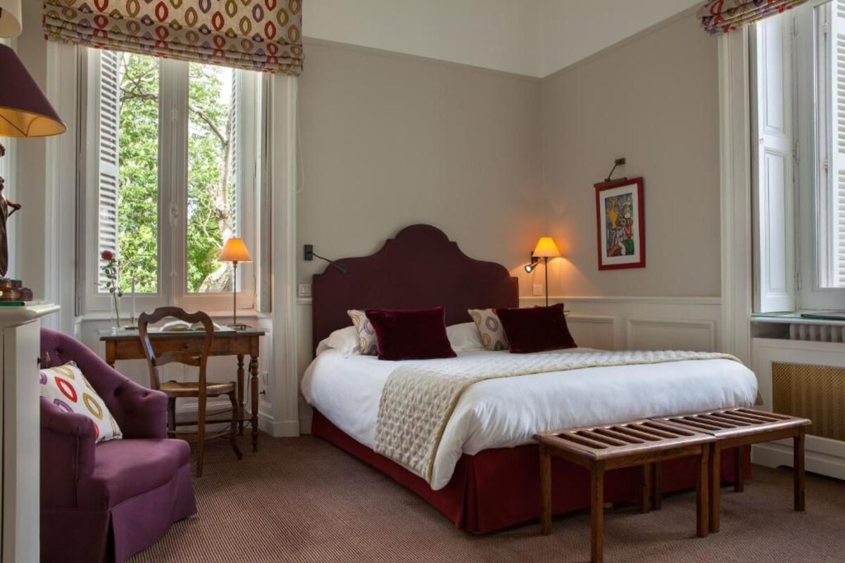 A bedroom with a large bed, a desk, a chair, and a bench.