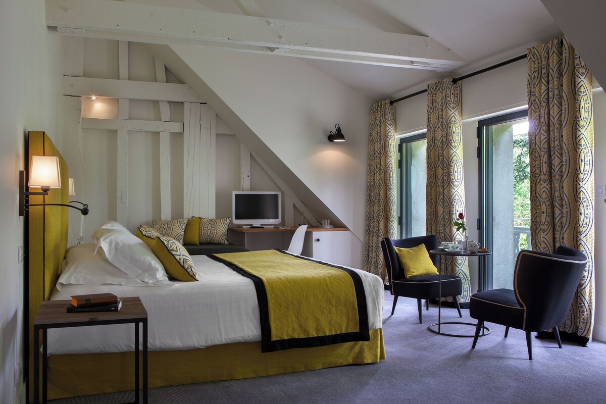 A hotel room with a bed, a desk with a computer, a chair, and a small table with a vase.