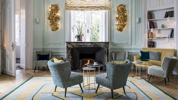 Una habitación con chimenea, dos sillones, un sofá, una estantería y una alfombra estampada.