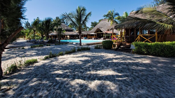 Um resort com piscina, construções de palha e uma praia de areia.