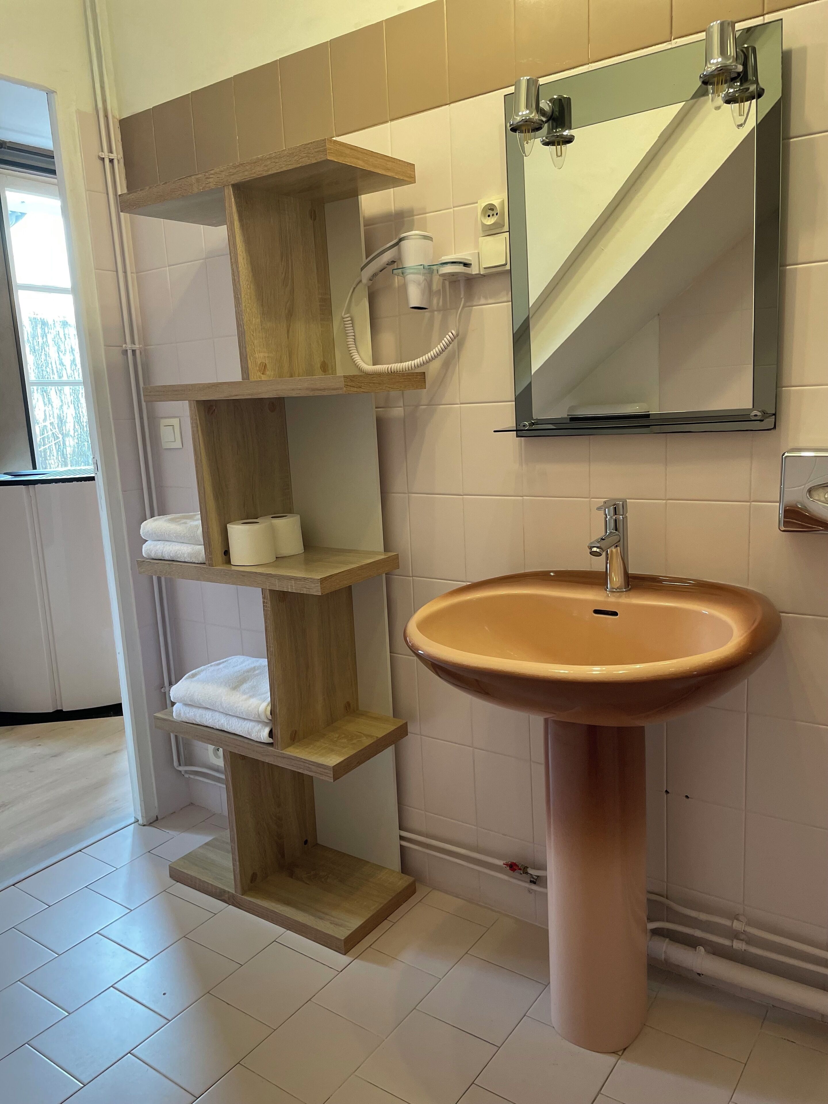 Un baño con un lavamanos color crema, repisas de madera, un espejo y un perchero para toallas.