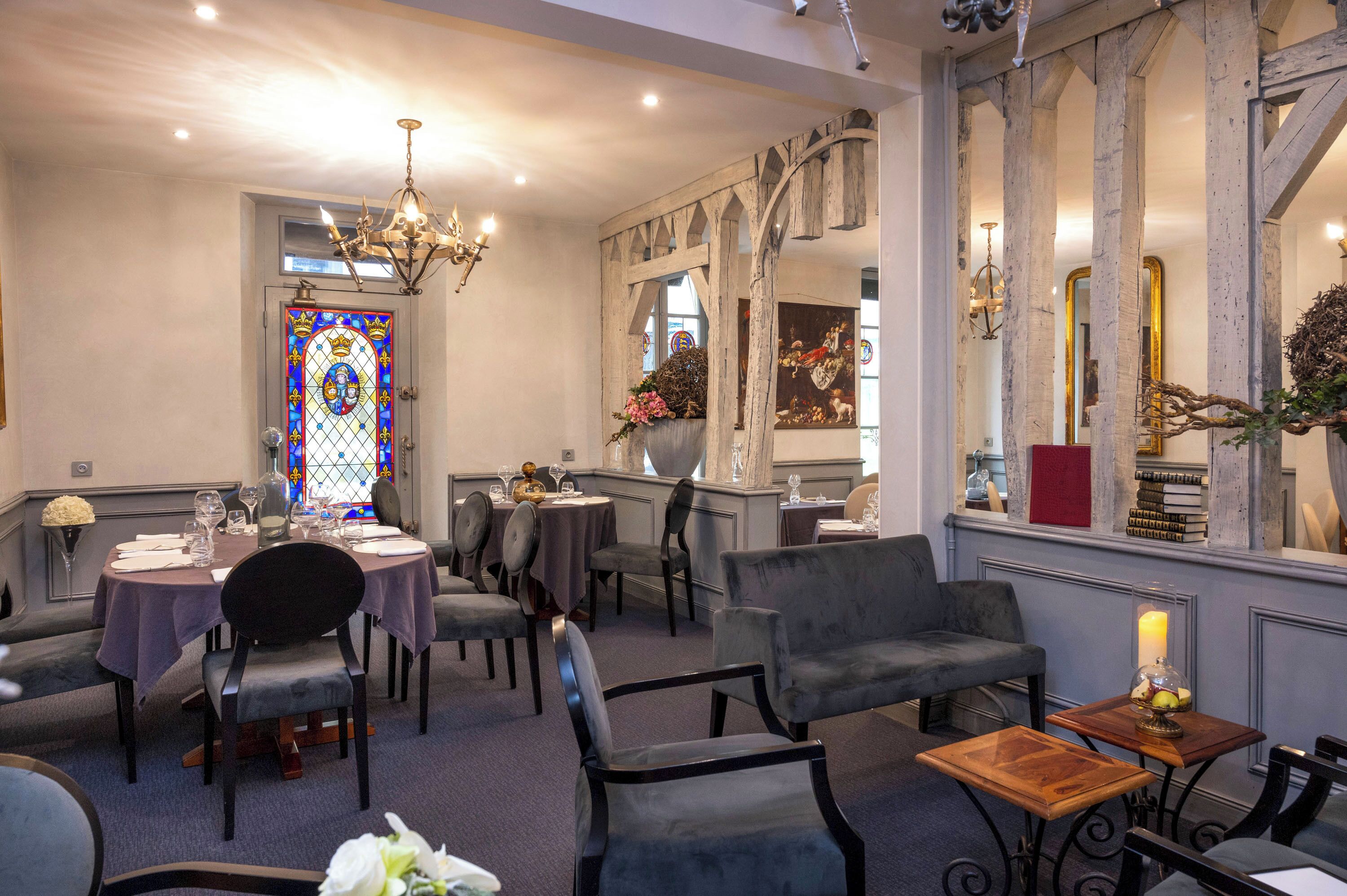 A dining area with round tables, chairs, a chandelier, and a stained glass window.