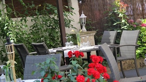 Un área de comedor al aire libre con mobiliario de mimbre, una mesa preparada con copas y cubiertos, y un farol.