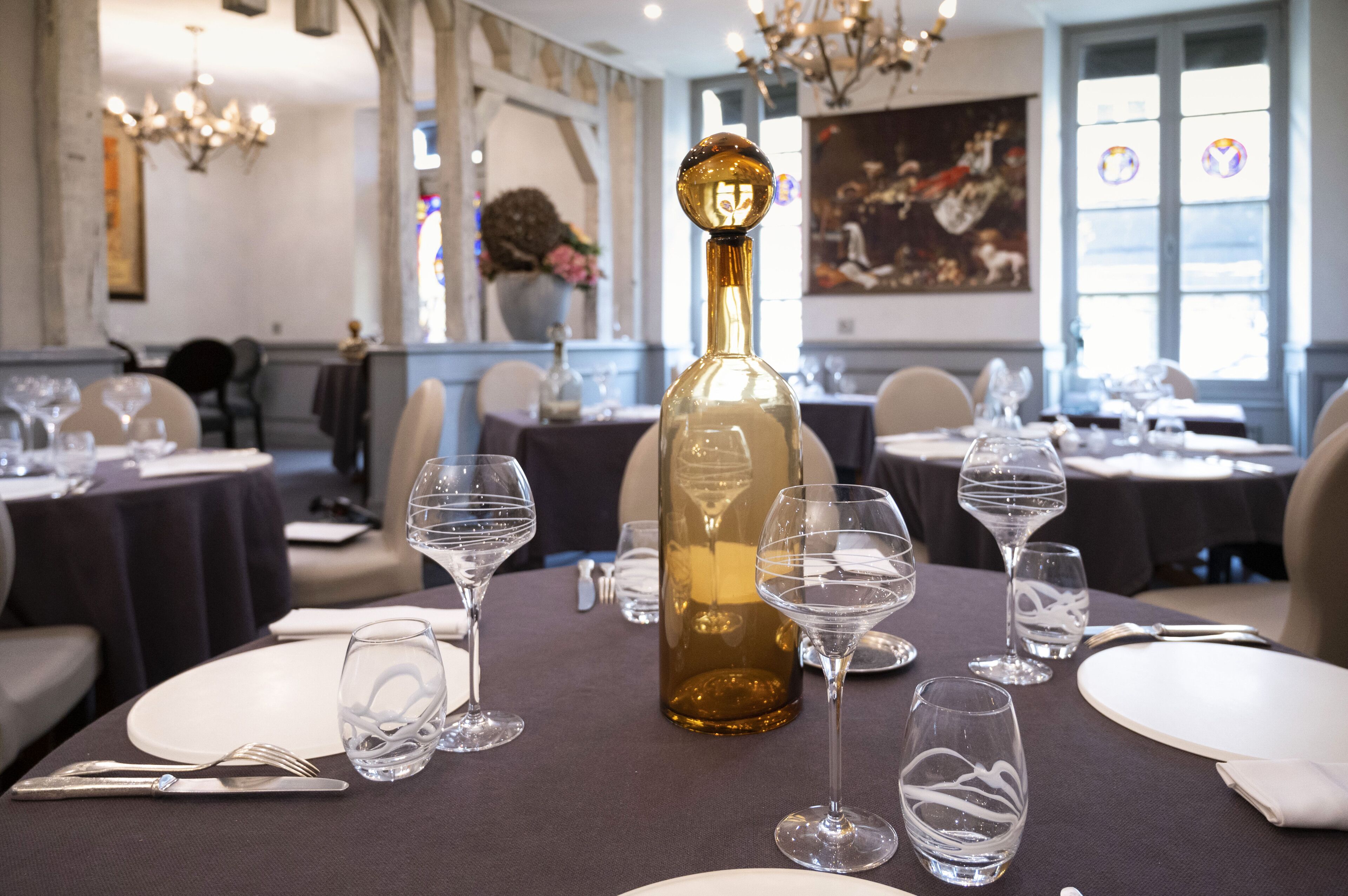 Une table dressée dans un restaurant, avec des verres à vin, une bouteille et des couverts, le tout sous des lustres et entourée d’œuvres d’art accrochées aux murs.