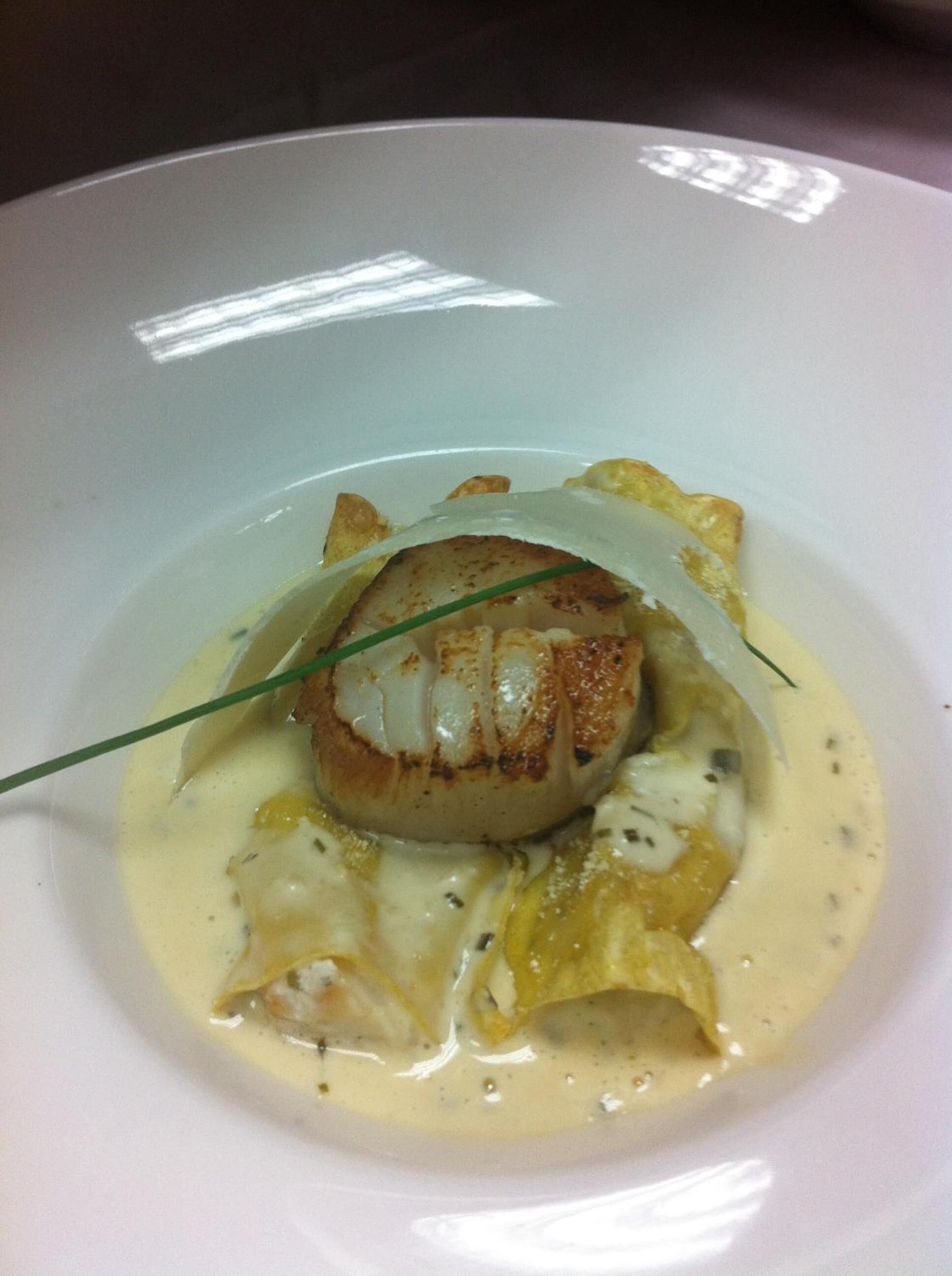 Ein Teller mit einem gebratenen Scallop, einer cremigen Soße und Gemüse.