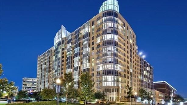 A multi-story hotel with a curved facade, large windows, and a prominent cylindrical top section. - Weichert Suites at Wisconsin Place (Chevy Chase)