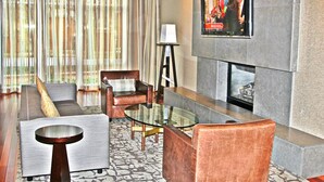 A modern hotel lobby with a sofa, armchairs, a glass coffee table, a lamp, and a flat-screen TV mounted on the wall. - Weichert Suites at Wisconsin Place (Chevy Chase)