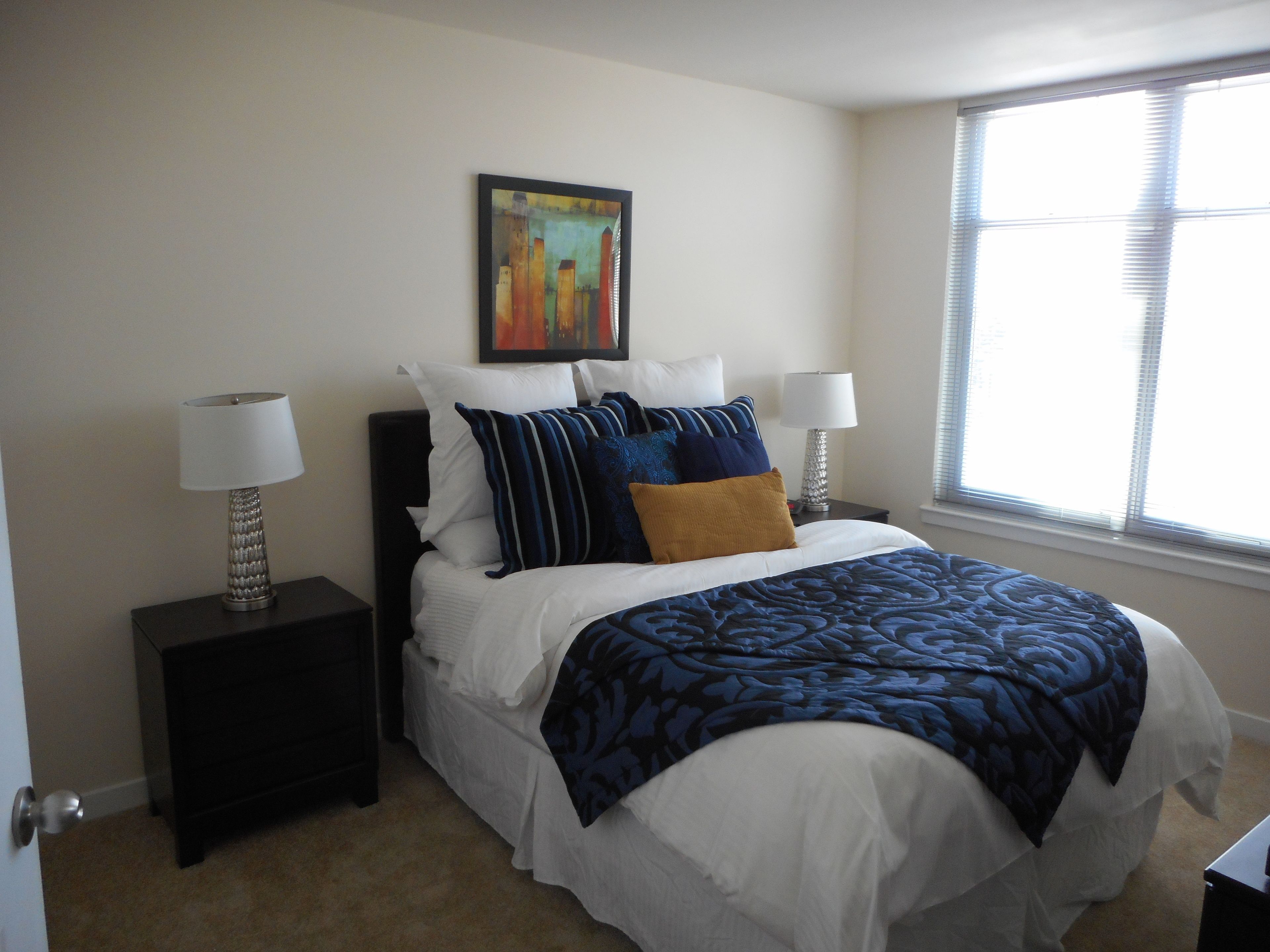 A neatly arranged bedroom with a bed, two bedside tables, a window, and a painting on the wall.