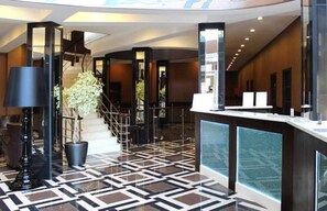 Un hall d’hôtel moderne avec un sol à motifs géométriques, un comptoir d’accueil et un escalier.