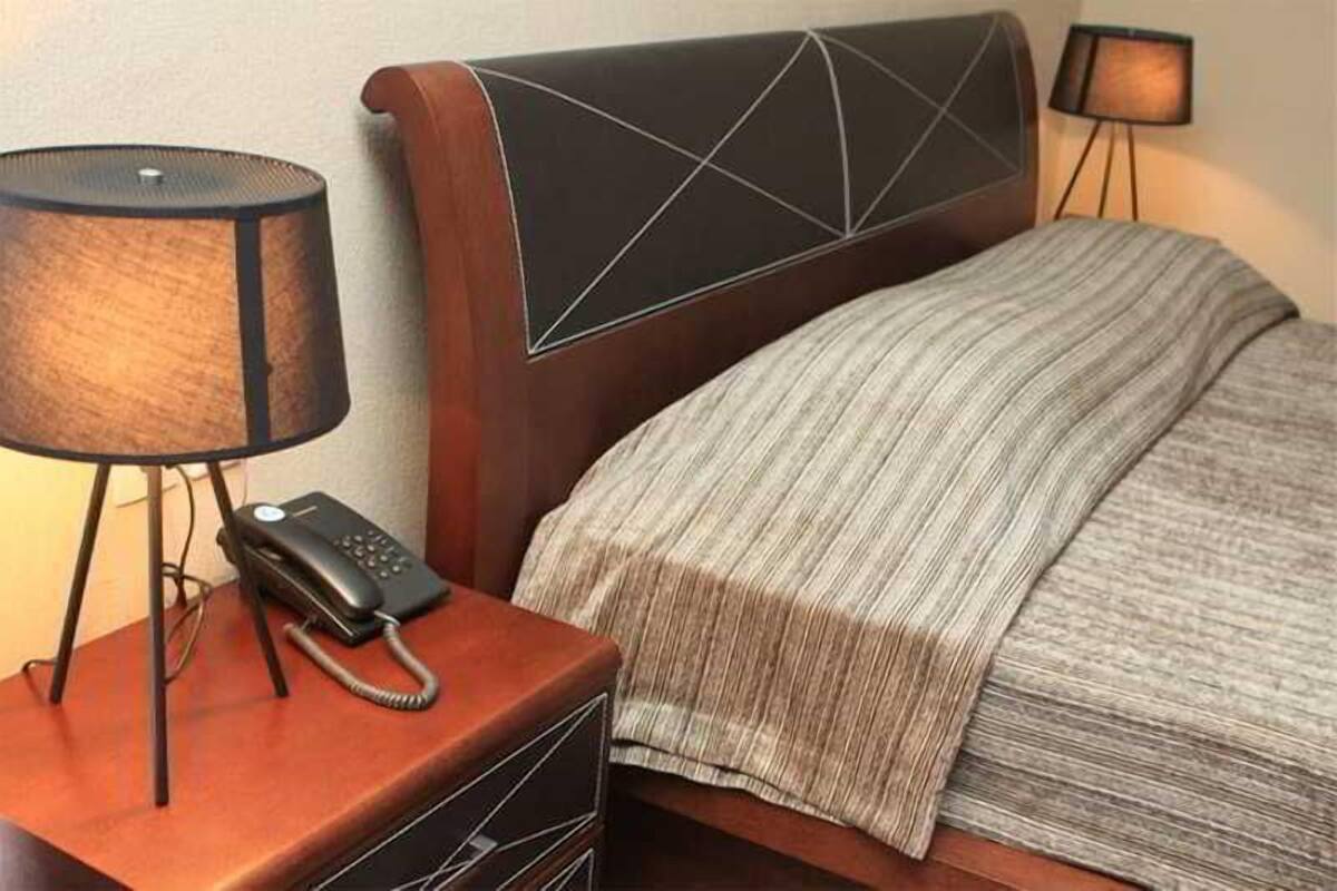 A hotel room with a bed, a bedside lamp, a telephone, and a nightstand.