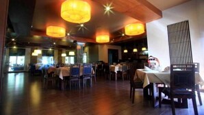 Un restaurant amb diverses taules, bigues de fusta al sostre i llums penjants.