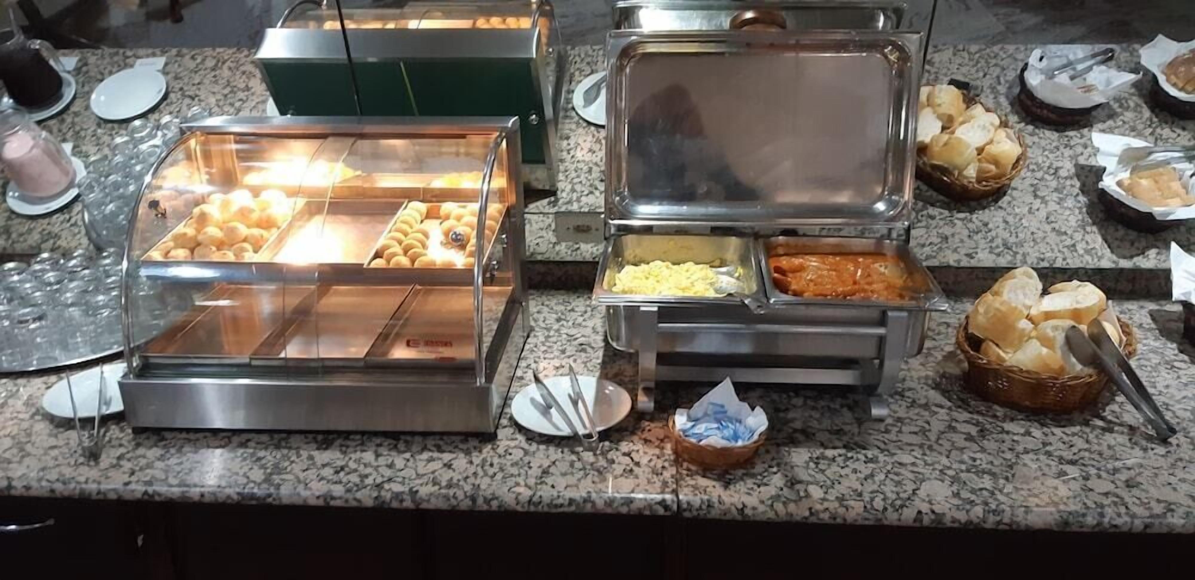 Buffet com diversos alimentos, incluindo pães e pastelaria, sobre uma bancada de granito.
