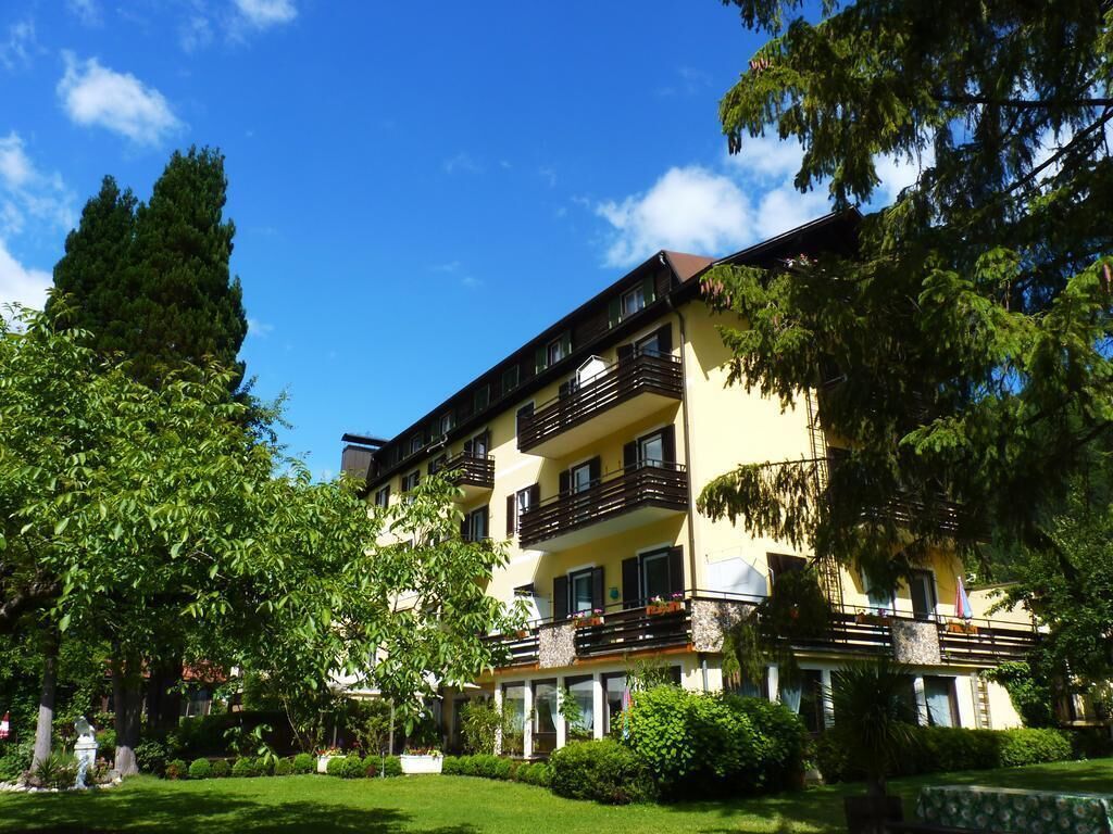 A multi-story hotel with balconies, a well-maintained lawn, and surrounding trees.