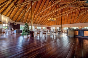 A spacious indoor area with a high wooden ceiling, wooden flooring, and a Christmas tree. - Hakusembe River Lodge (Rundu)