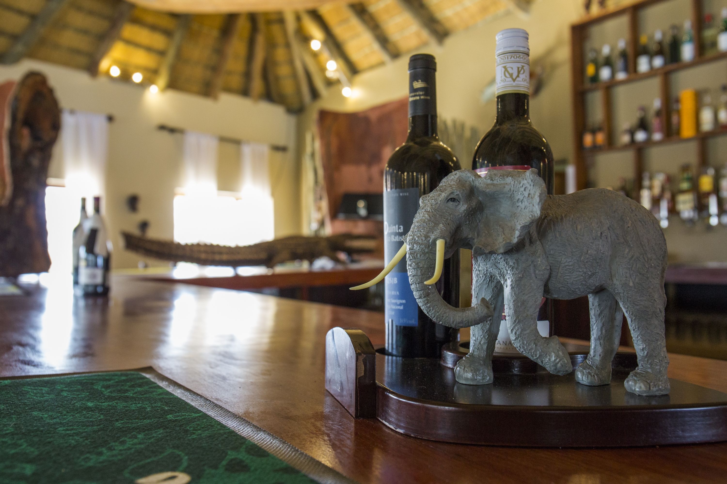 A bar area with a wooden counter, a decorative elephant sculpture, and bottles of wine.