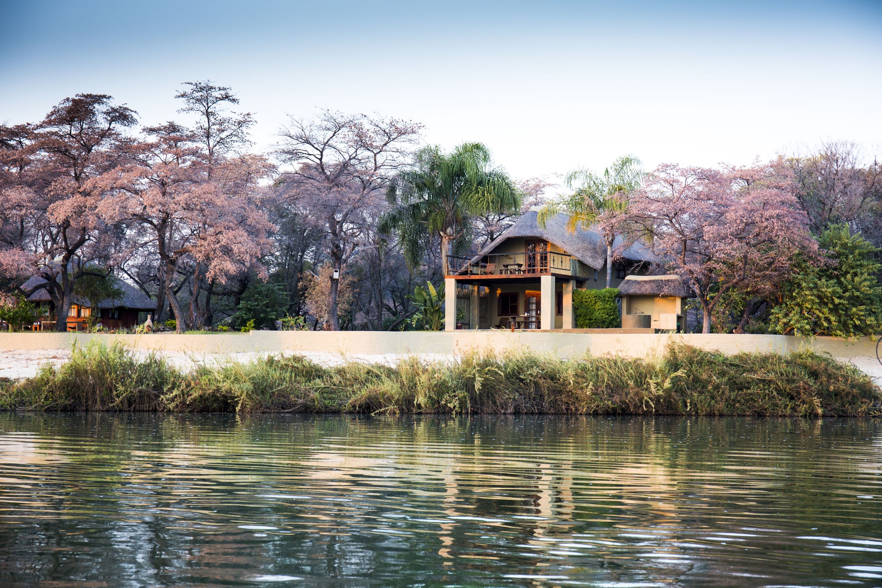 A lakeside property with a thatched-roof building, surrounded by trees and a calm water body.