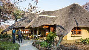 A thatched-roof building with a reception area and a paved walkway leading to it.