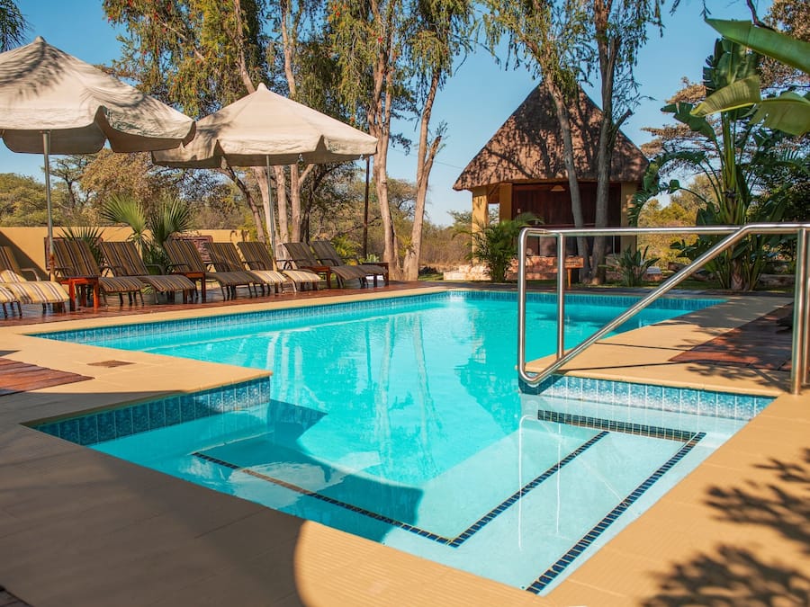 Una piscina con trampolín, sillas de descanso y sombrillas.