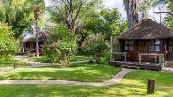 A bungalow with a thatched roof, surrounded by lush greenery and flowering plants.