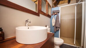 A bathroom with a wooden vanity, a white sink, a mirror, a towel rack, and a shower area.
