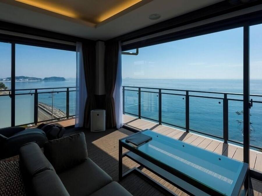 A balcony with a glass table and chairs, overlooking the sea.