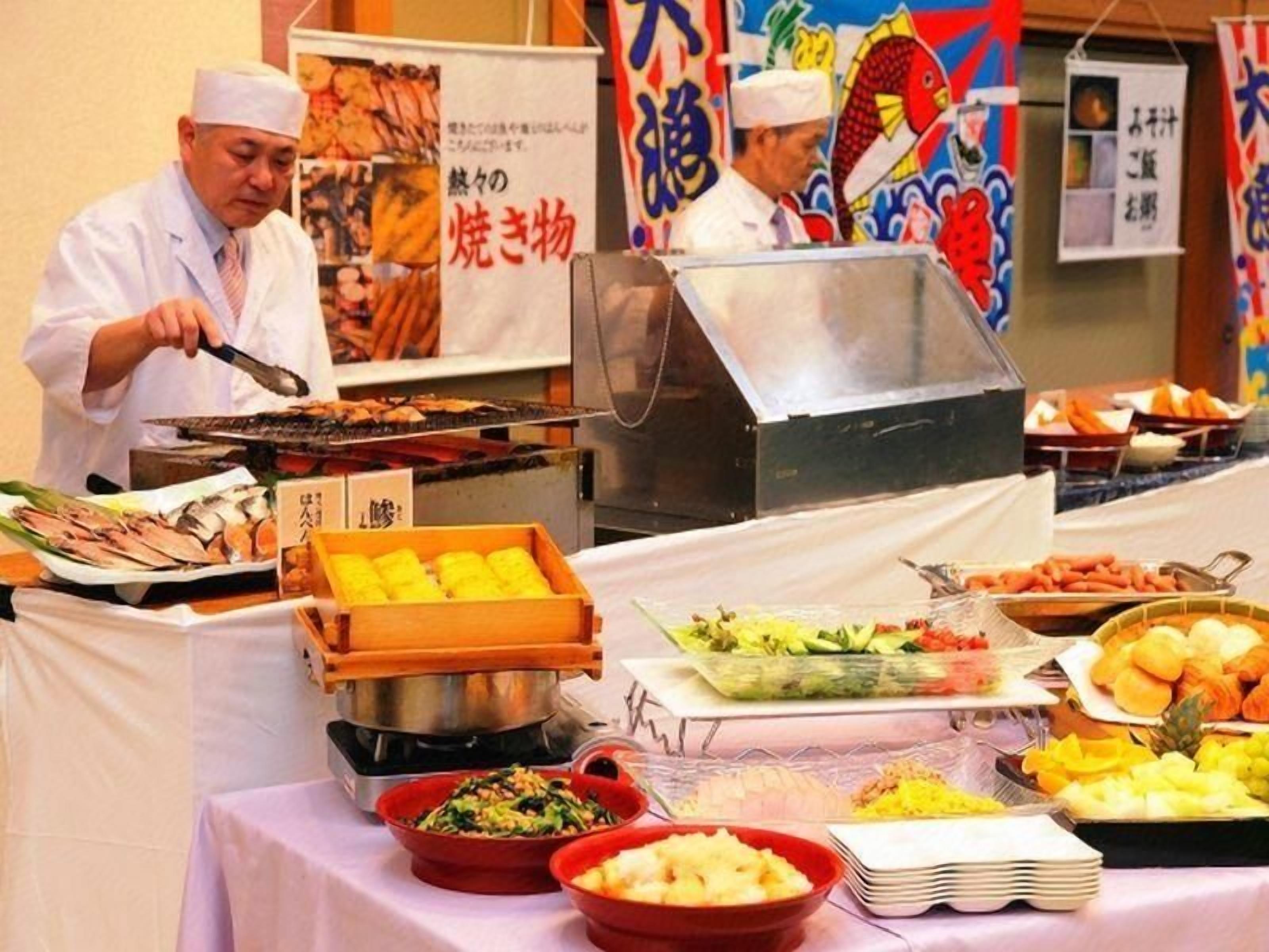 A buffet setup with various food items and a person grilling.